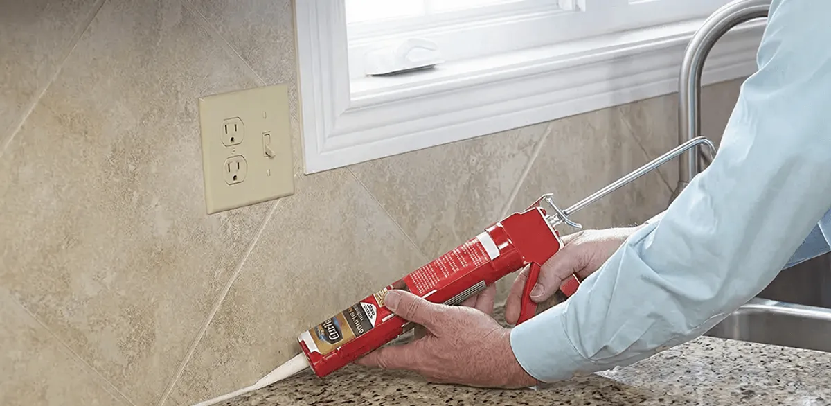 Handyman applying caulk along a kitchen backsplash and countertop seam in Tuscaloosa, AL
