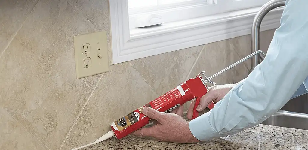 Handyman applying caulk along a kitchen backsplash and countertop seam in Tuscaloosa, AL