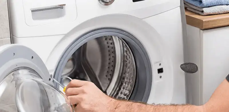 Handyman repairing a front-load washing machine and inspecting the drum in Tuscaloosa, AL